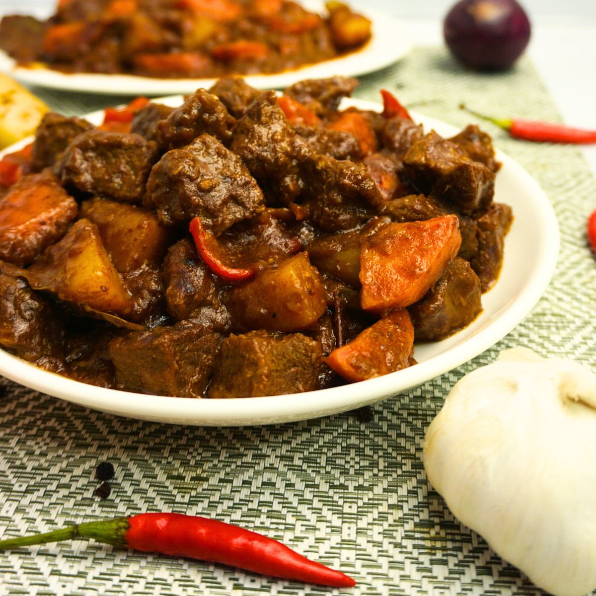 Close up view of a plate of beef caldereta with fresh chilis, garlic and onion on the table.