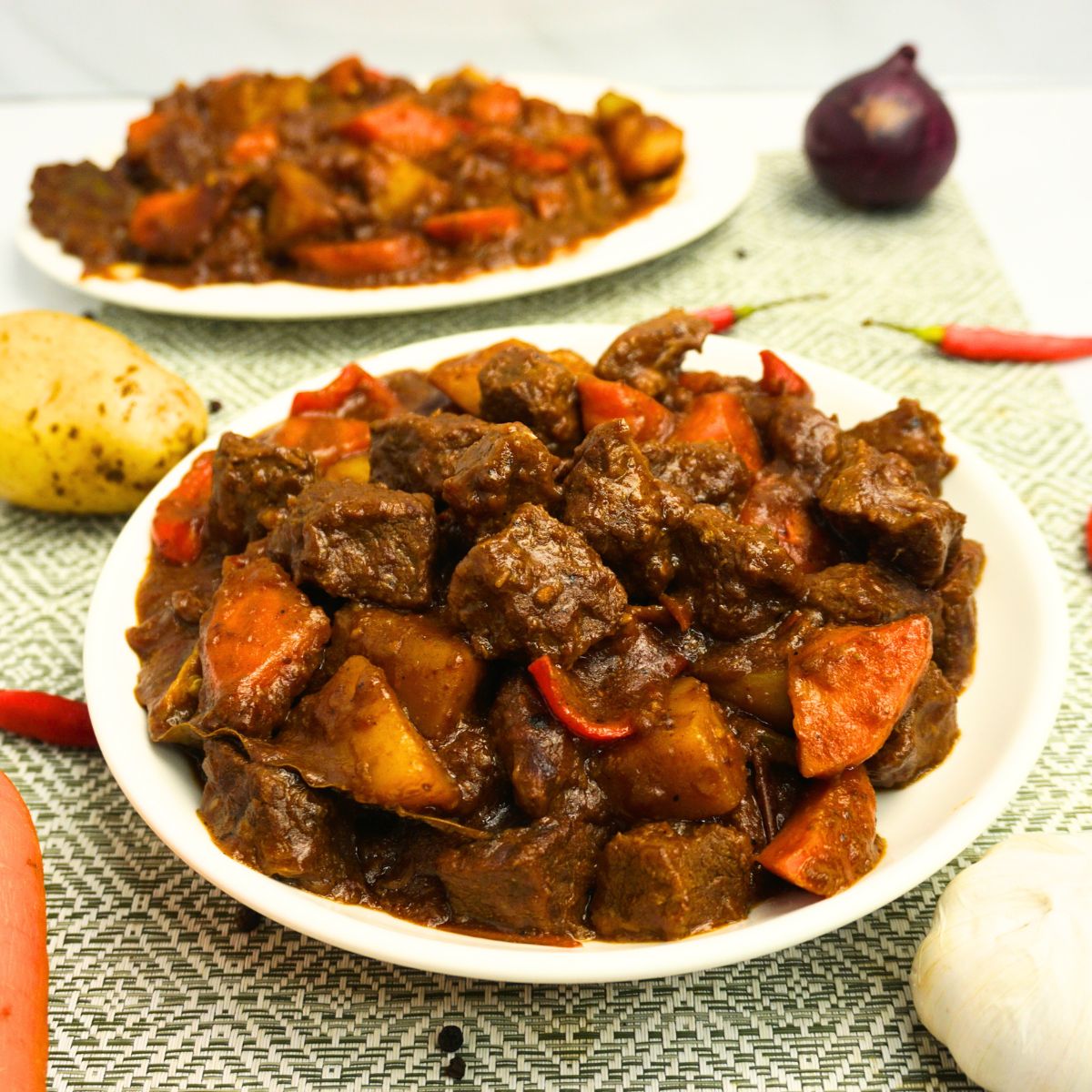 Spicy beef caldereta serve on plates with fresh ingredients on the side.