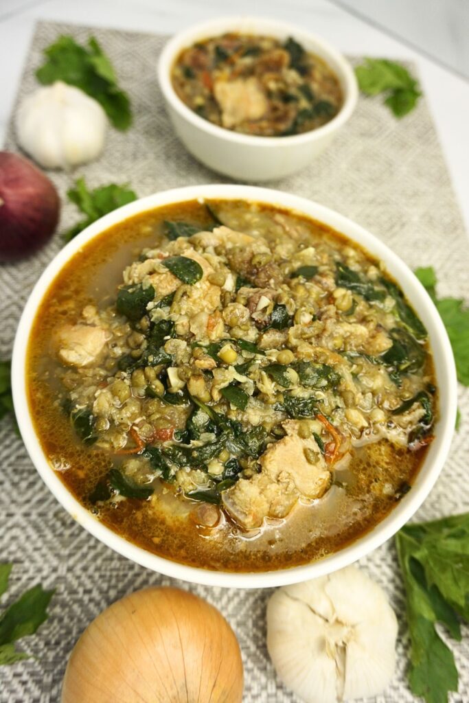 Bowl of ginisang monggo with garlic, onions ampalaya leaves on table.