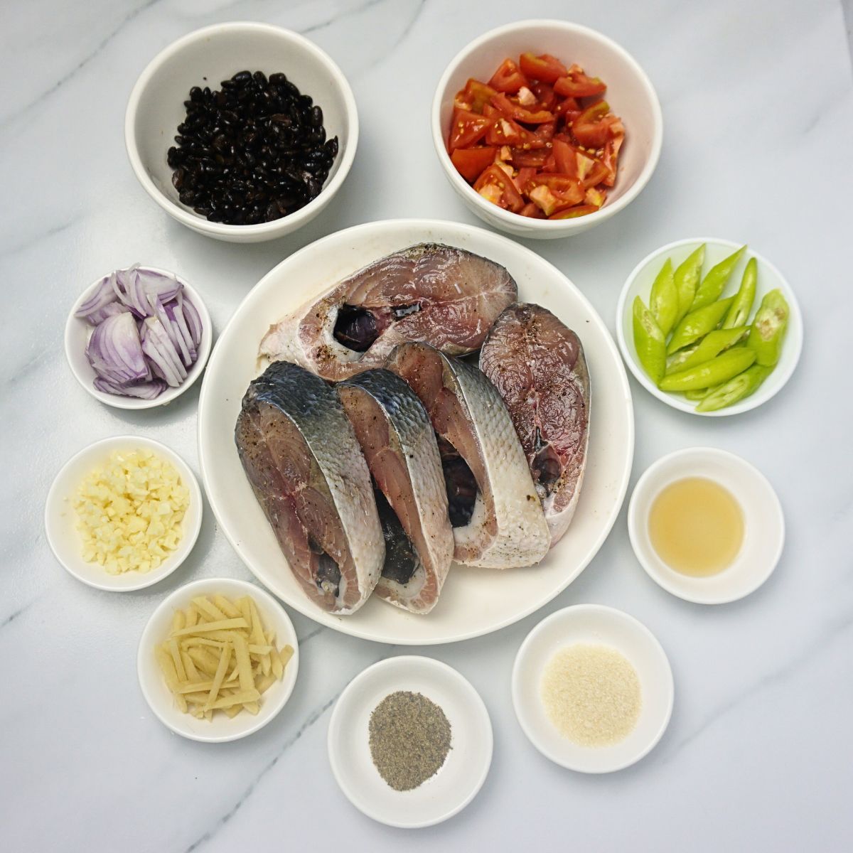 Bangus with tausi ingredients in bowls. Bangus belly, ginger, garlic, onion, tausi, tomatoes, green chilies, fish sauce, black pepper and cooking oil.