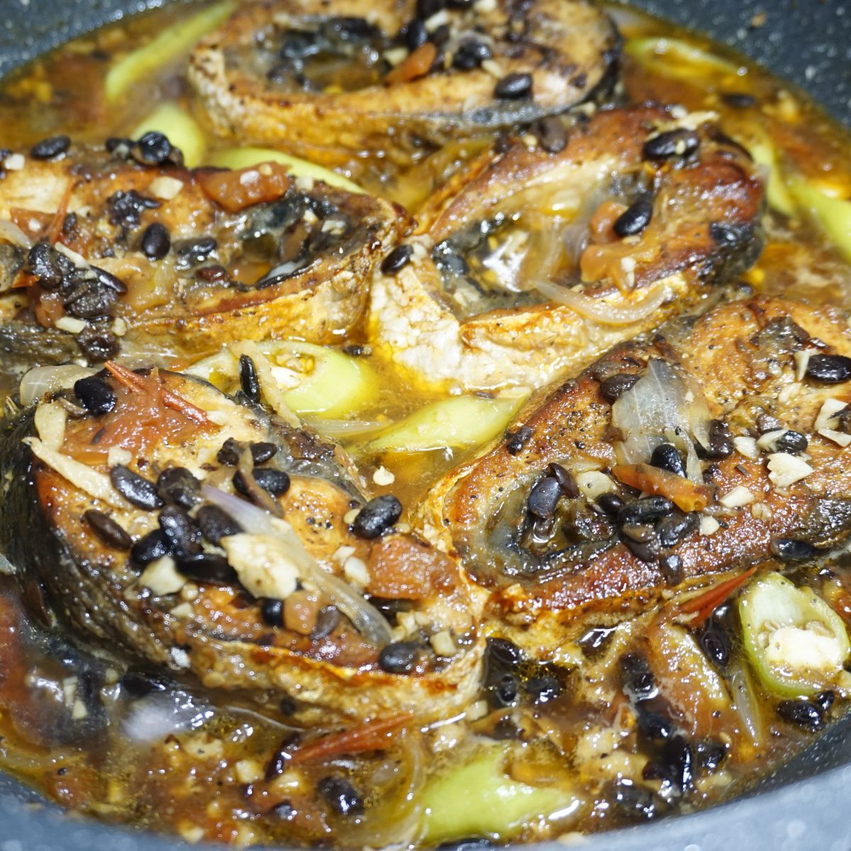 Bangus belly cooked in tomatoes and black beans in a pan.