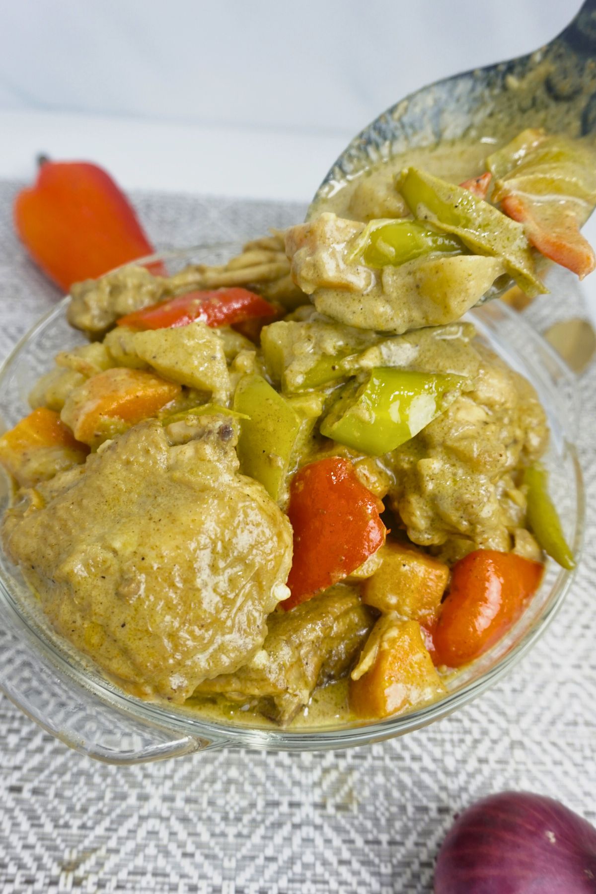 Ladle pouring chicken curry sauce with vegetable in a bowl.