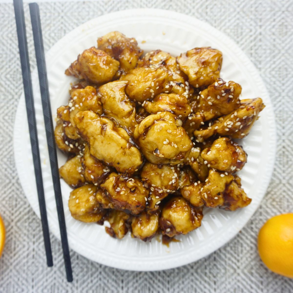 Plate of orange chicken in a plate with wooden chopsticks.