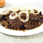 Plate of bistek tagalog with fresh calamansi and onions on a table.