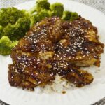 Plate of chicken teriyaki with steamed broccoli on the sides.