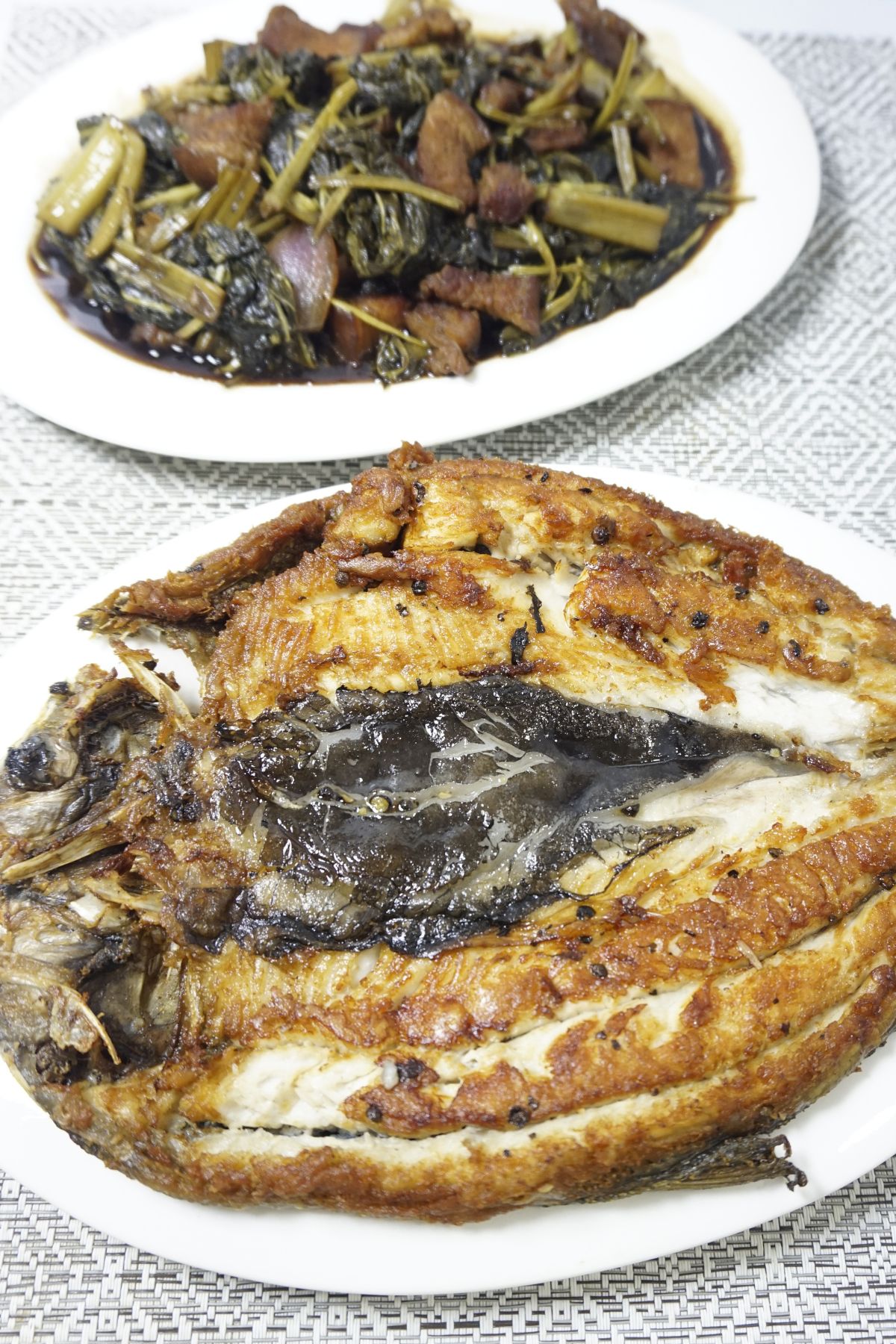 Fried daingna bangus served in a white plate beside a serving of adobong kangkong.